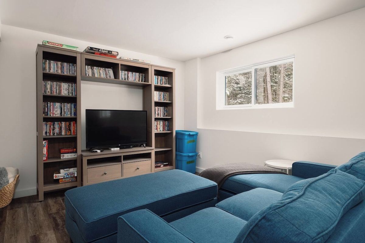 Una sala de estar con un televisor de pantalla plana, una estantería, un sofá azul y un ventanal con vistas a árboles.