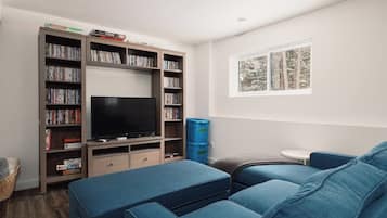 Una sala de estar con un televisor de pantalla plana, una estantería, un sofá azul y un ventanal con vistas a árboles.
