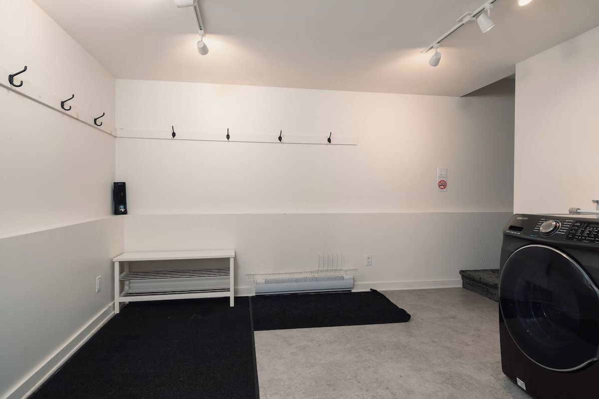 A laundry room with a washing machine, a drying rack, a bench, and a wall-mounted drying rack.