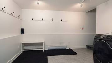 A laundry room with a washing machine, a drying rack, a bench, and a wall-mounted drying rack.