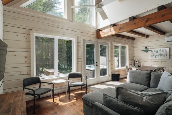 A cozy cabin interior with a wooden interior, large windows, a dining area, and a sofa.