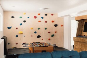 A room with a climbing wall, a foosball table, and a wooden cabinet. - Spa, Climbing Wall & Arcade ~ Biking & Golf! (Saint-Faustin-Lac-Carré)