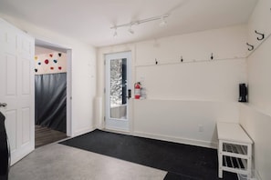 A hallway with a white door, a coat rack, a small white table, and a black mat at the entrance.