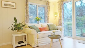 A cozy living room with a white sofa, a small side table, a potted plant, and a vase with flowers.