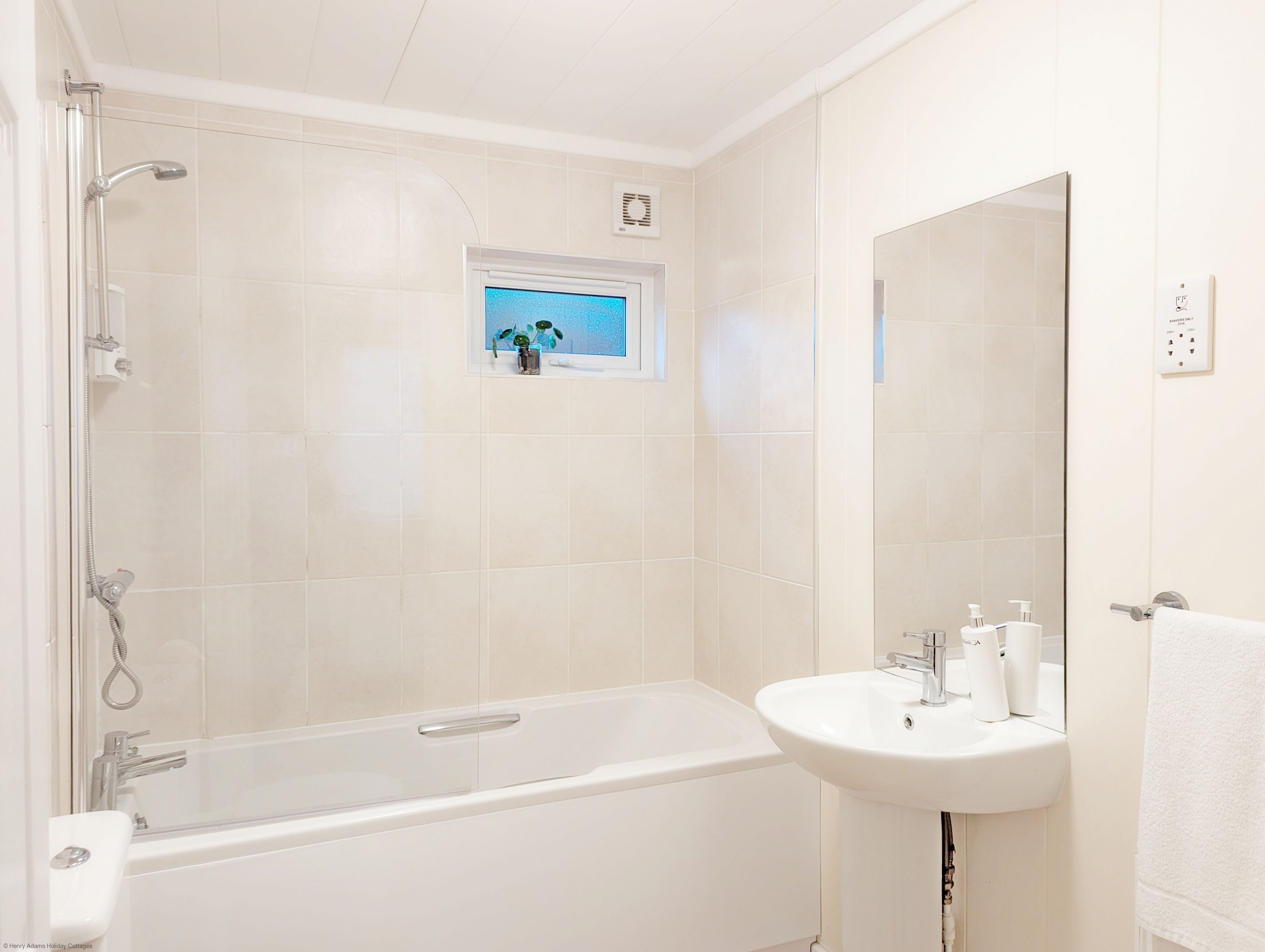 A bathroom with a bathtub, a sink, and a window with a view of the sky.