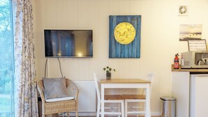 A cozy room with a wicker chair, a wooden table, and a television on the wall.