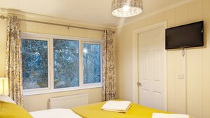 A bedroom with two beds, a television, and a window with curtains.