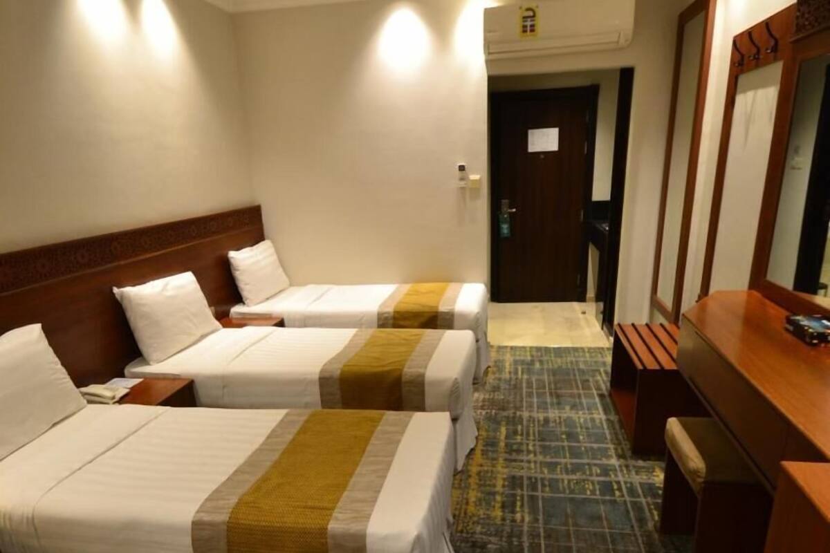 Hotellihuone, jossa on kolme erillistä sänkyä, puinen työpöytä ja peili.