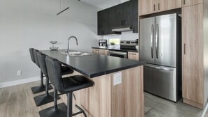Una cocina moderna con una isla central, taburetes negros, electrodomésticos de acero inoxidable y armarios de madera.