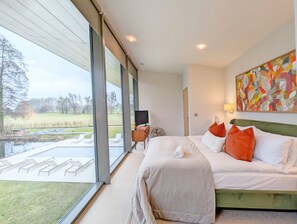 Een moderne hotelkamer met een groot bed, een flatscreen-televisie en uitzicht op een tuin en vijver.