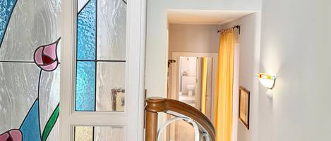 A hallway with a wooden handrail, a stained glass window with floral designs, and a sign reading 'B&B See the Sea'.
