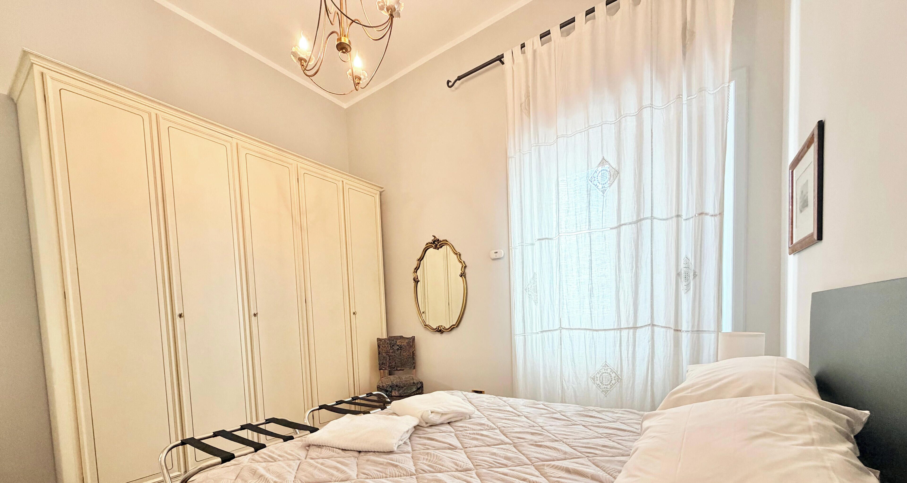 A bedroom with a bed, a wardrobe, a mirror, and a window with curtains.