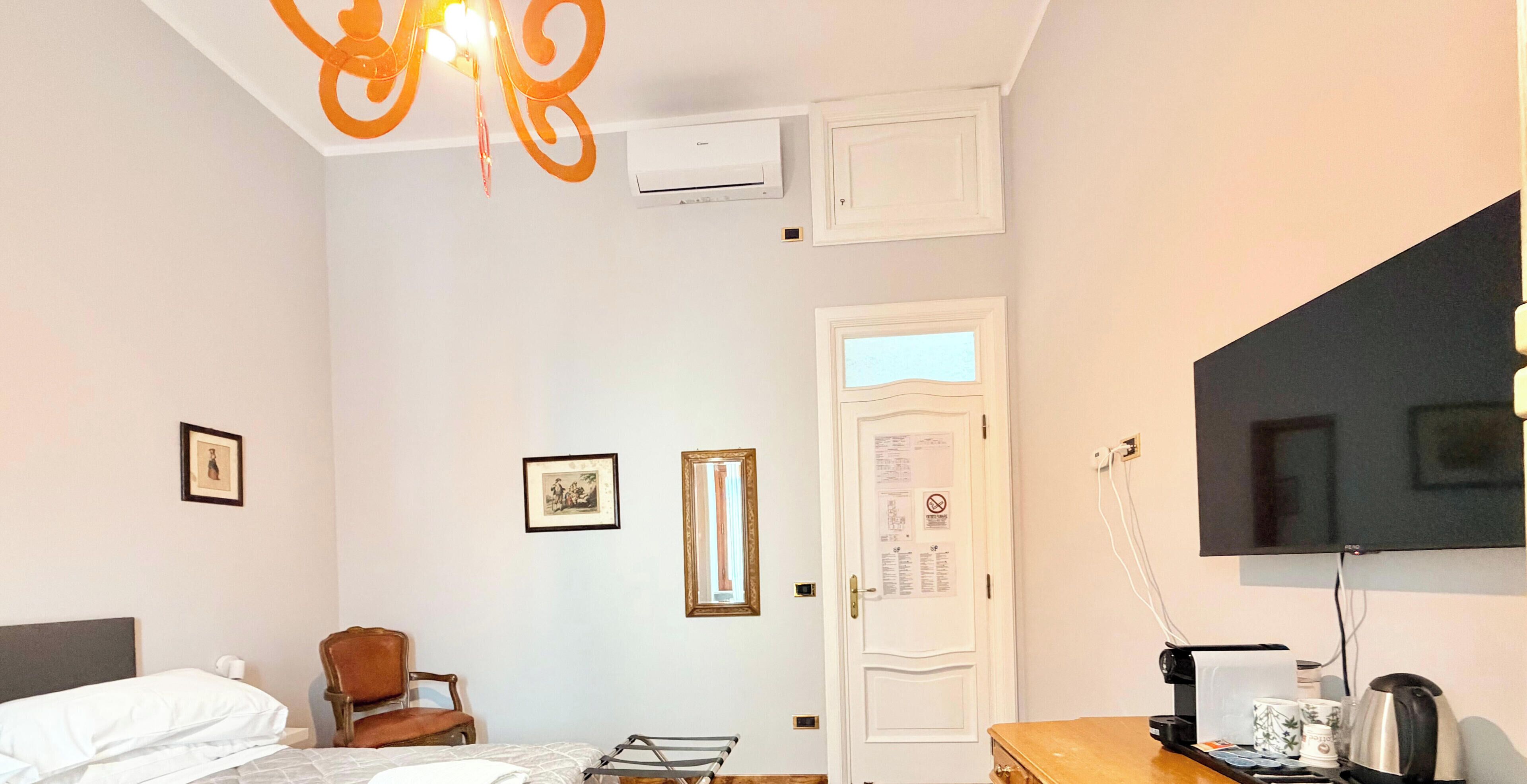 A hotel room with a bed, a chair, a desk with a television, and an air conditioning unit.