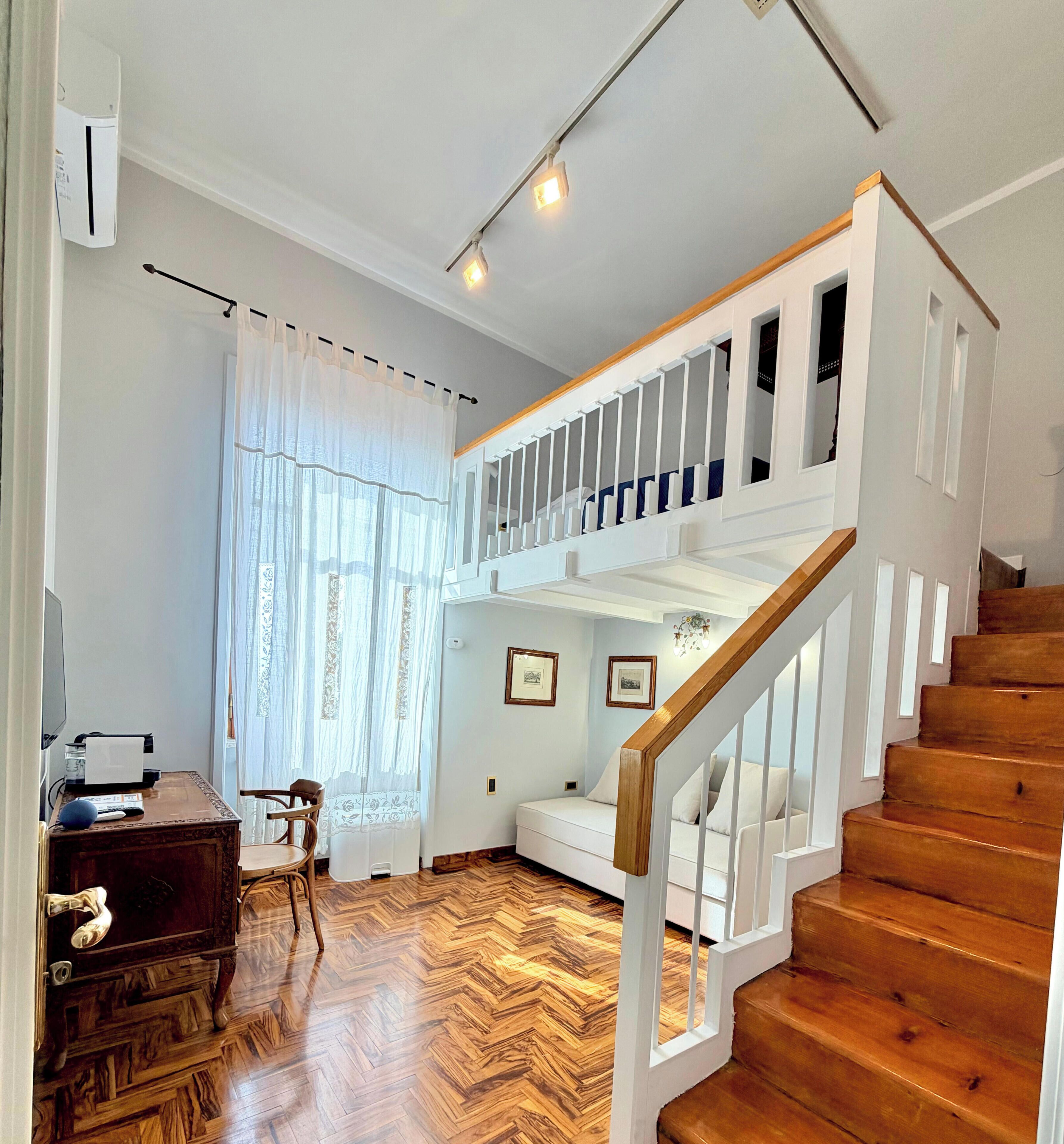 A spacious room with a wooden herringbone floor, a white staircase with a wooden handrail, and a ceiling light fixture.