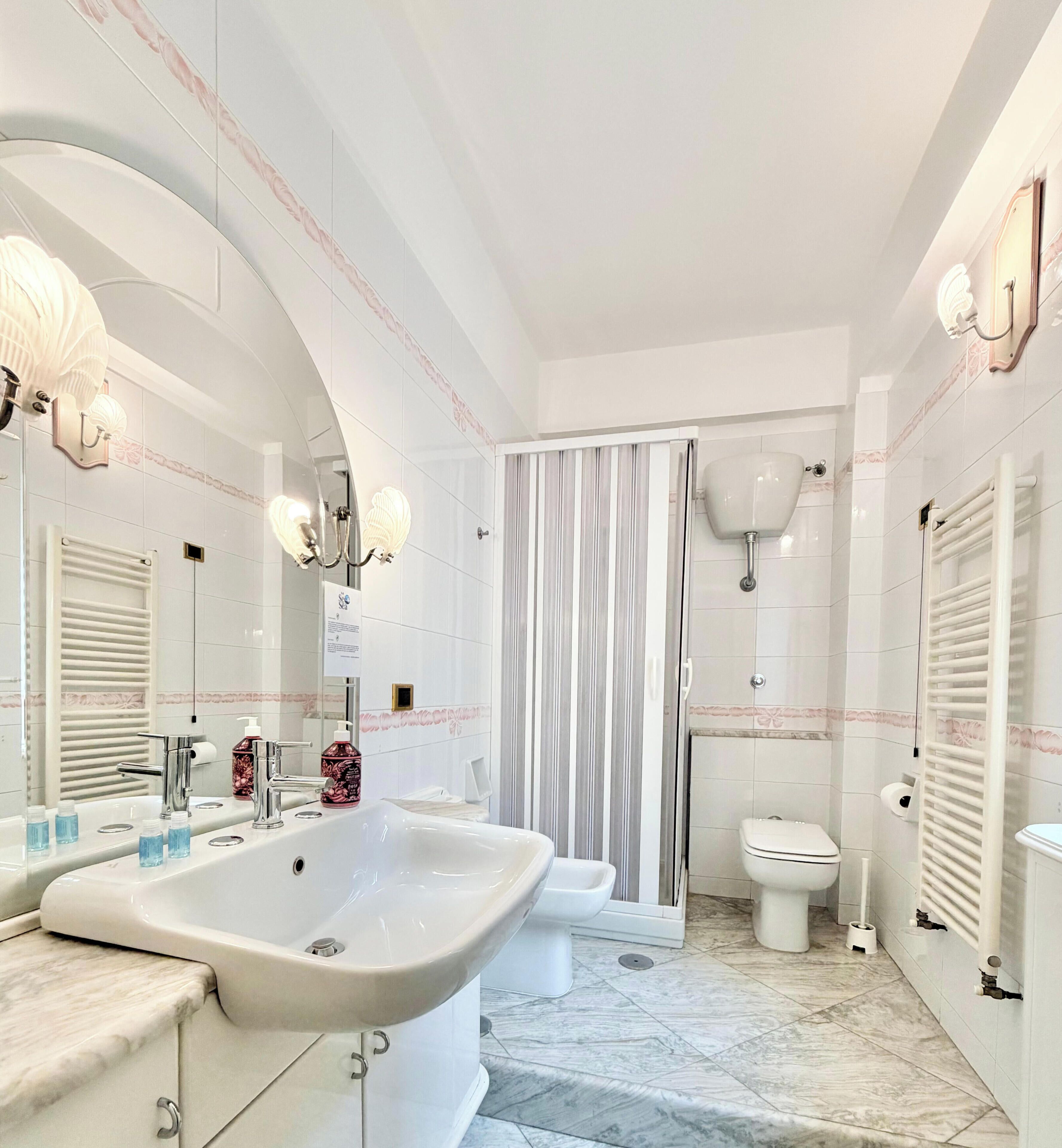 A modern bathroom with a large sink, a toilet, a shower area, and a mirror with wall sconces.