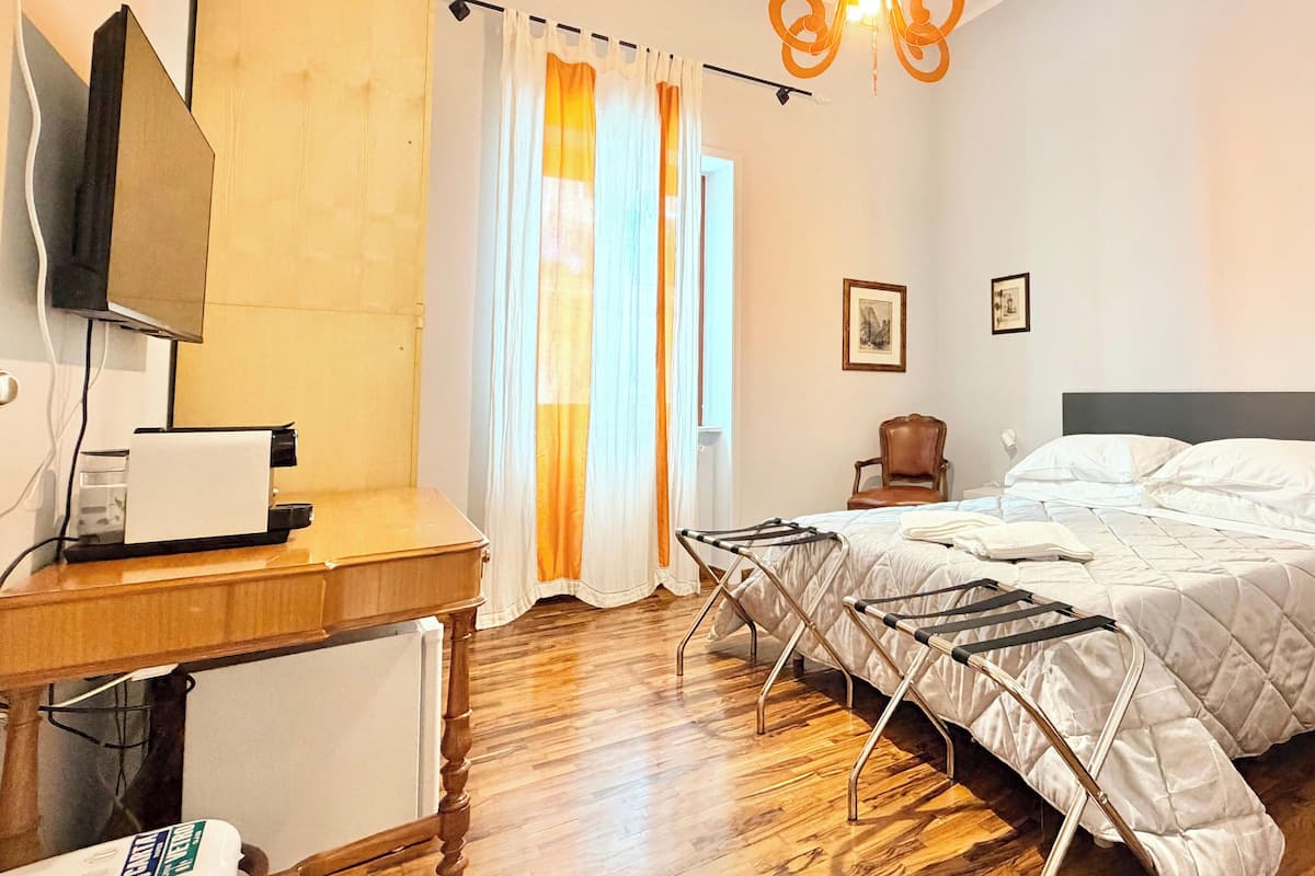 A hotel room with a wooden floor, a bed with white bedding, a desk with a television, and a hanging light fixture.