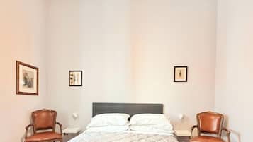 A hotel room with a bed, two chairs, a nightstand, and a ceiling light fixture.