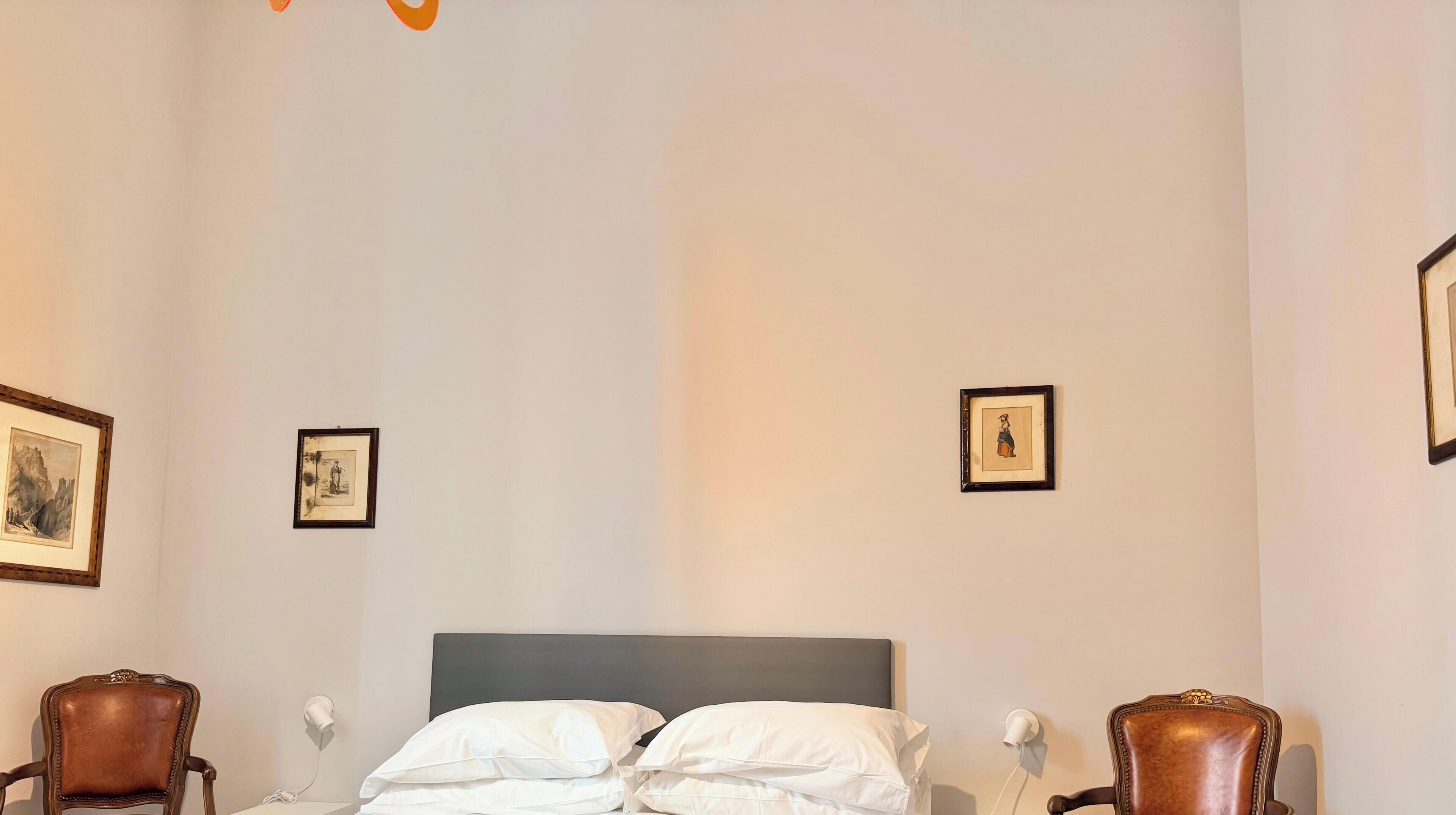 A hotel room with a bed, two chairs, and two framed pictures on the walls.