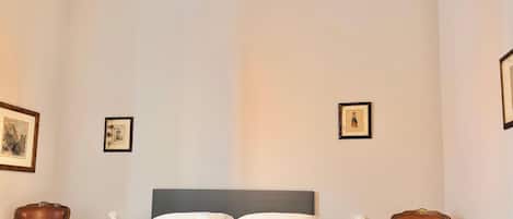 A hotel room with a bed, two chairs, and two framed pictures on the walls.