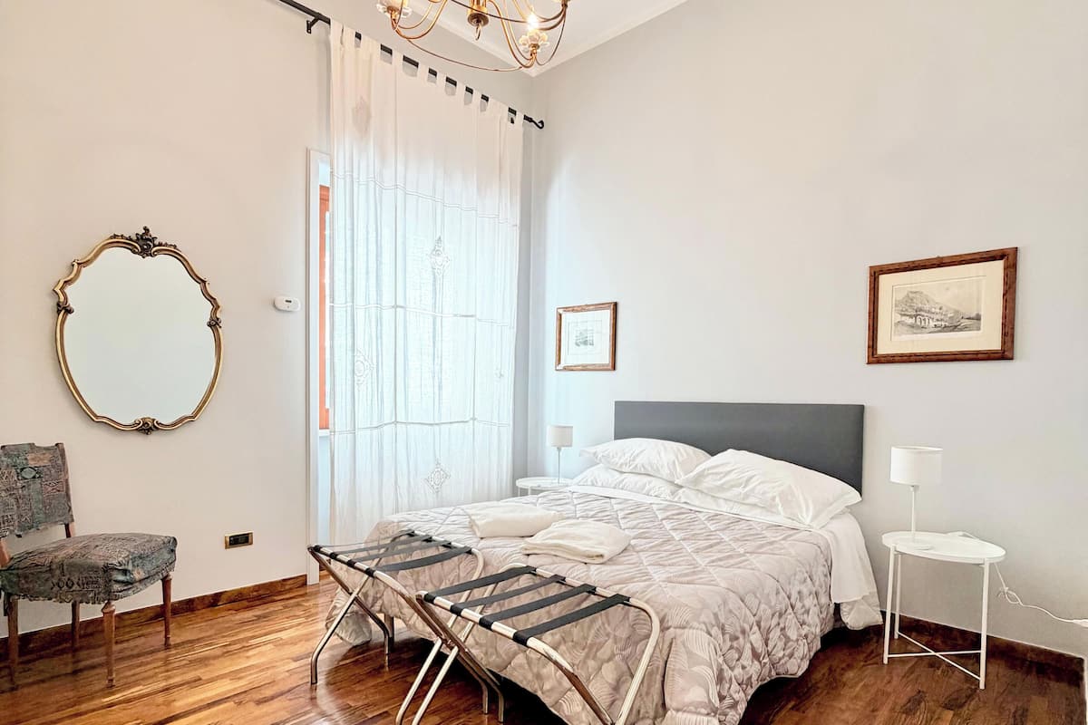 A bedroom with a bed, a chandelier, a chair, a mirror, and a small table.