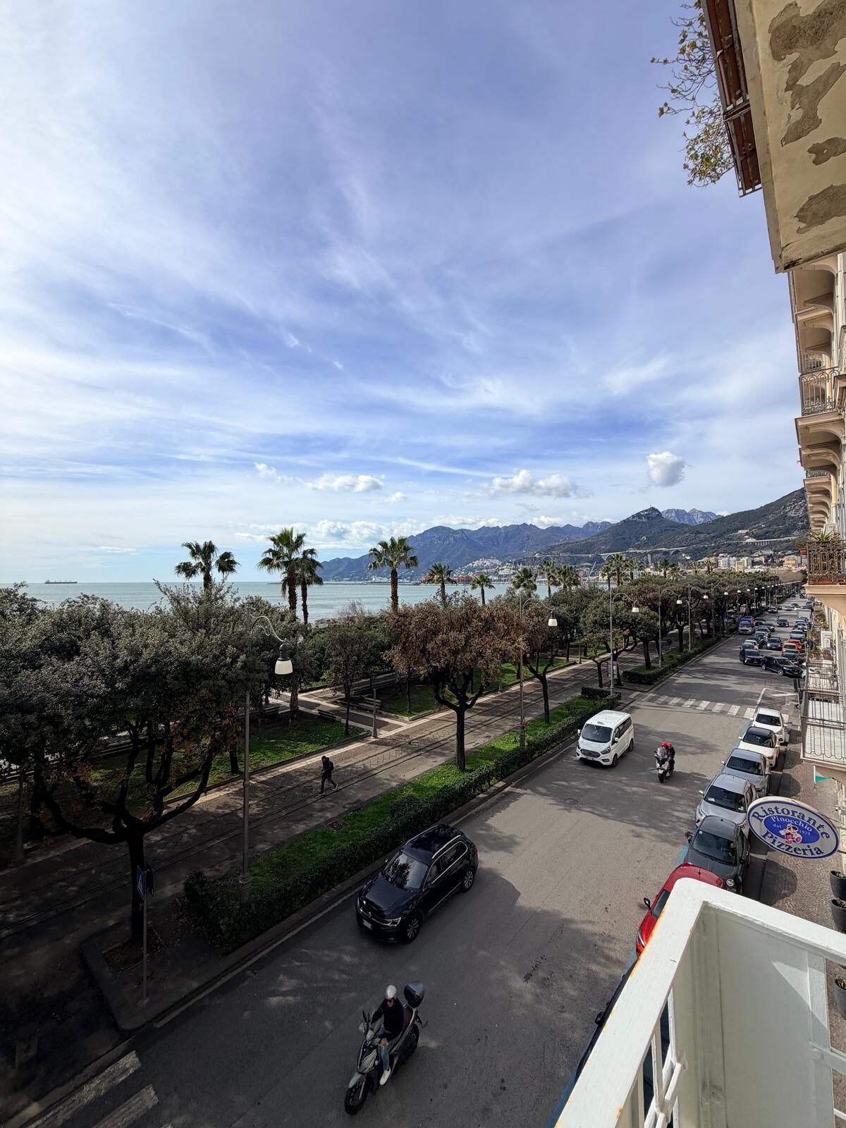 A street view with parked cars, a motorcyclist, and a pedestrian.