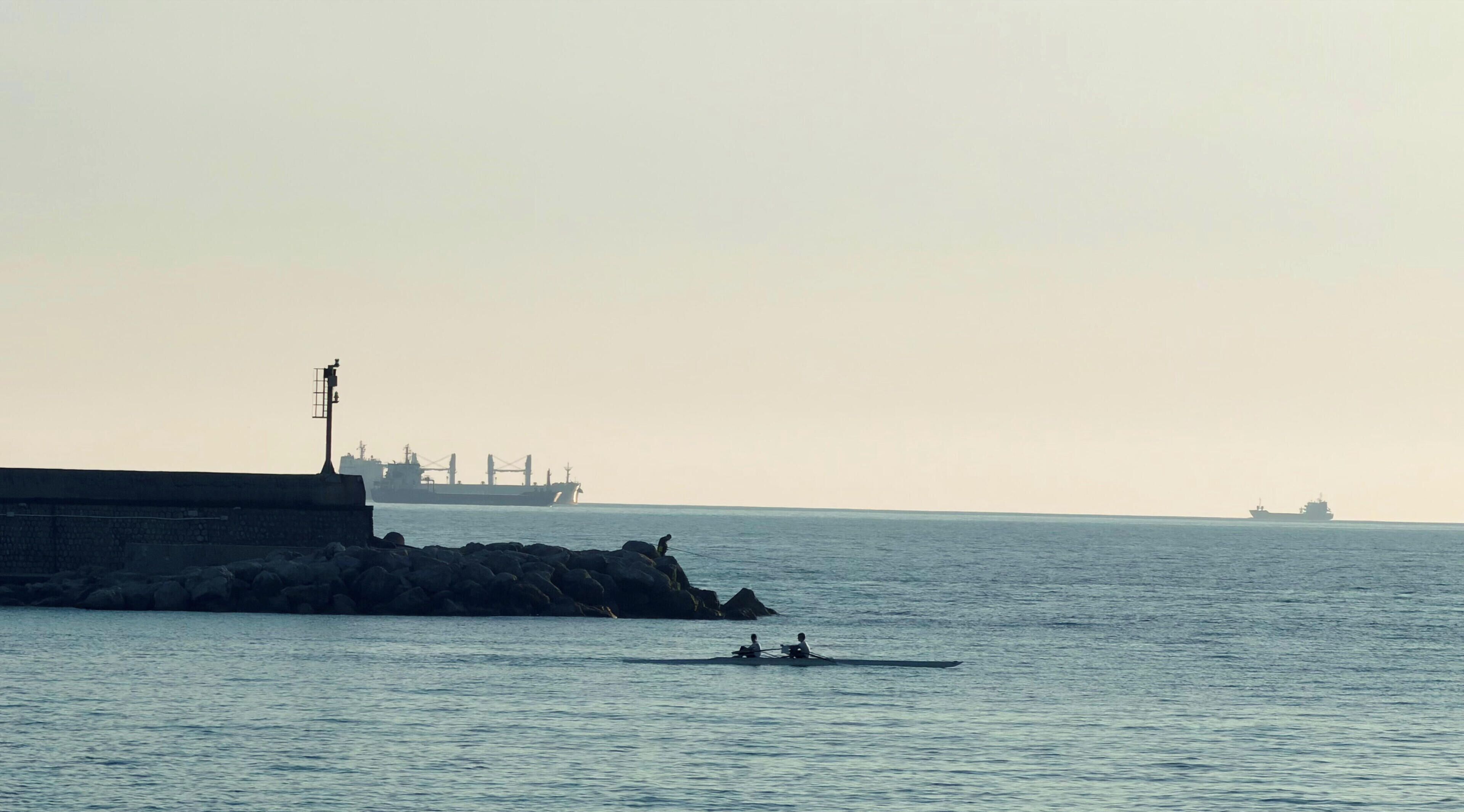 Une scène côtière avec une jetée, un grand navire de transport de marchandises et un plus petit bateau sur l’eau.