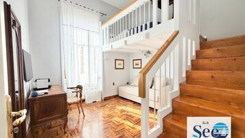 A room with a herringbone floor, a wooden staircase, a white sofa, and a desk with a computer.