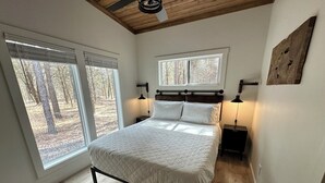 A bedroom with a bed, two bedside tables, a ceiling fan, and large windows with a view of trees. - Cozy Cypress Cabin (Mount Vernon)