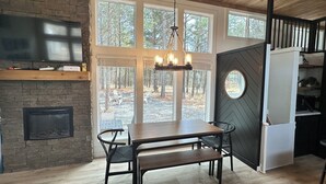 A modern kitchen with a large window, a built-in fireplace, and a dining area with a bench. - Cozy Cypress Cabin (Mount Vernon)