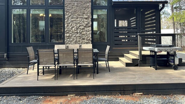 A modern outdoor patio with a stone wall, large windows, and a grill area. - Cozy Cypress Cabin (Mount Vernon)