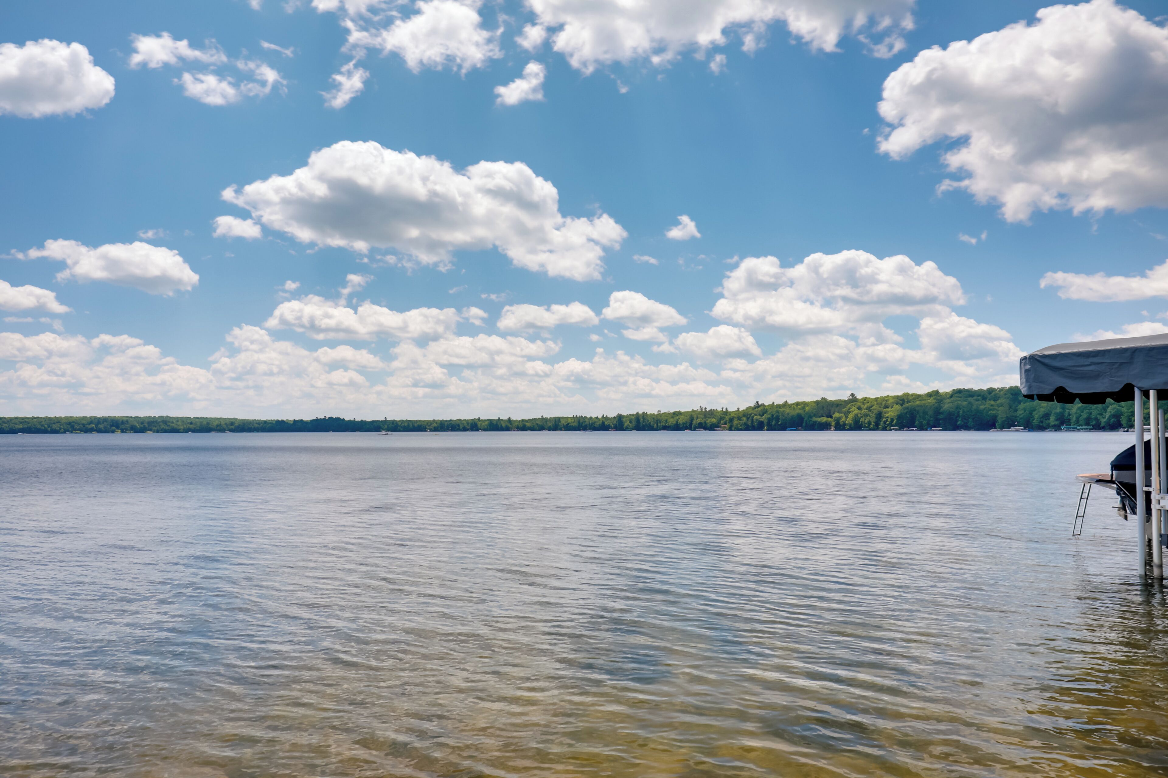 Um lago tranquilo com um píer e uma área coberta, ladeado por uma margem arborizada.
