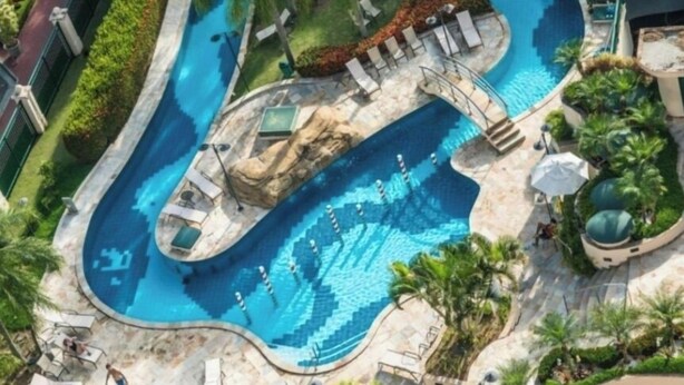 A large, winding pool with multiple lanes, surrounded by palm trees and lounge chairs. - Apart hotel Barra First  (Rio de Janeiro)