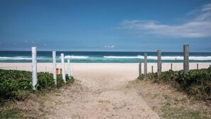 A sandy beach path leading to the ocean with a wooden fence on one side. - Apart hotel Barra First  (Rio de Janeiro)