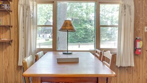 A dining area with a wooden table, chairs, a lamp, and a view through large windows. - South Twin Lake Cabin w/ Dock, Steps to Water (Conover)