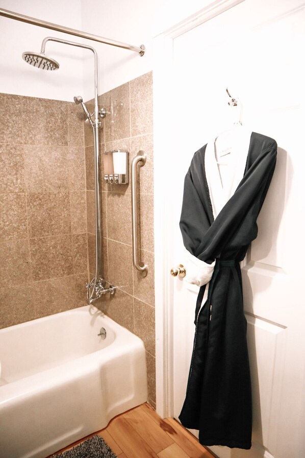 Un baño con bañera, ducha con cabezal de ducha manual y perchero con una bata colgada.