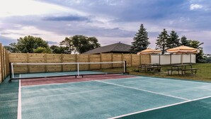 A tennis court with a net, surrounded by wooden fences and picnic tables.