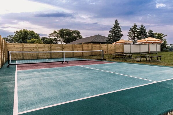 Cancha de tenis con red, rodeada de vallas de madera y mesas de picnic.