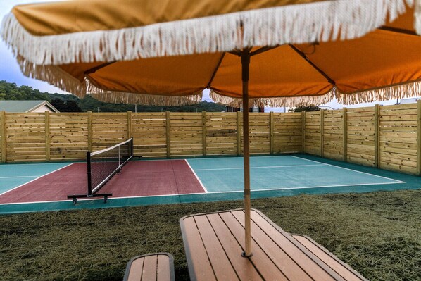 Una cancha de tenis al aire libre con valla de madera, una banca y una sombrilla.