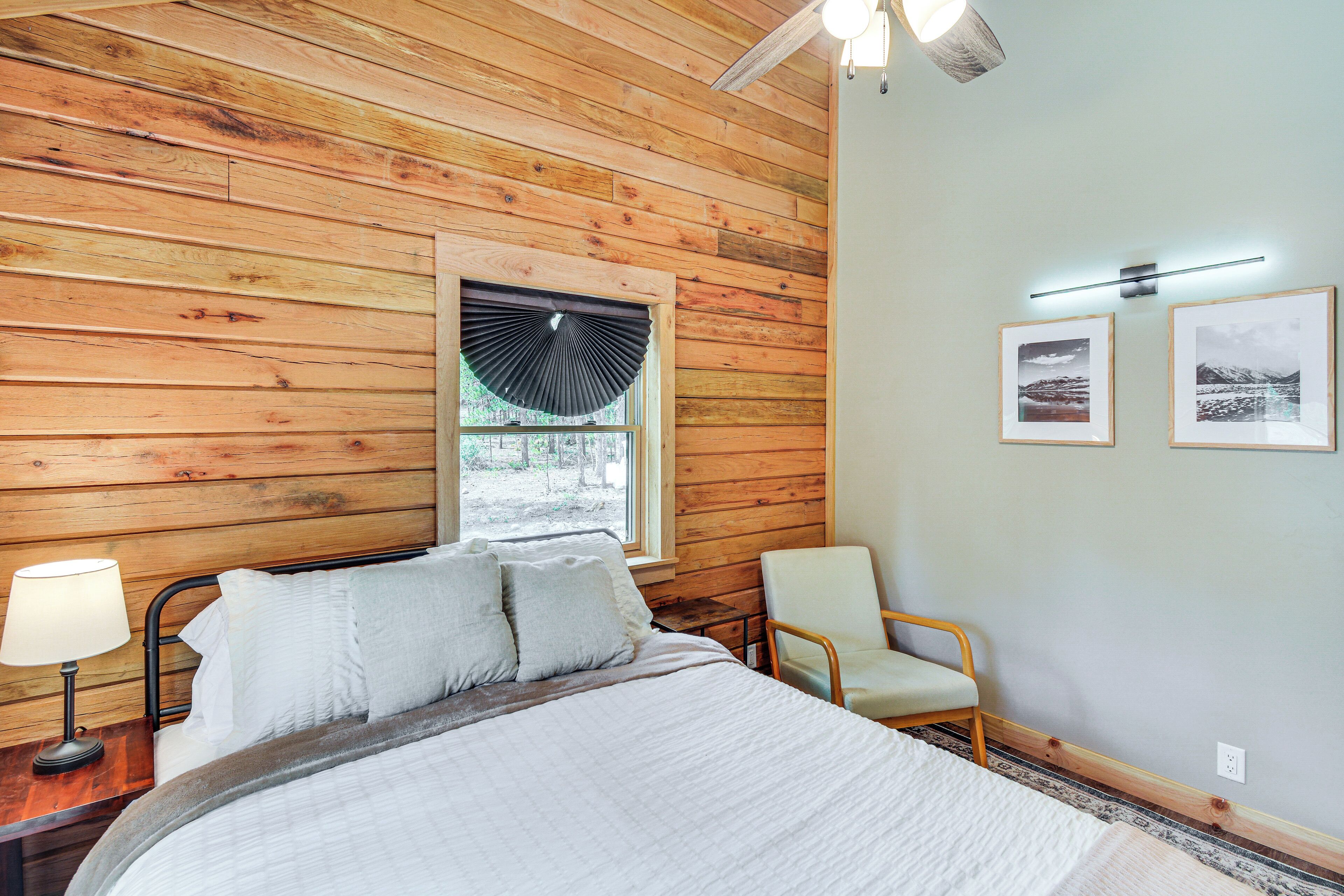 Un dormitorio con techo de madera, una cama con ropa blanca, una mesita de noche con lámpara, una silla y dos cuadros en la pared.