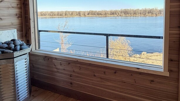 Una cabaña con un ventanal grande que ofrece vistas a un lago y un bosque.