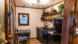Cocina compacta con estufa a gas, lavamanos y refrigerador. Hay una mesa de comedor con sillas y una lámpara colgante sobre ella.
