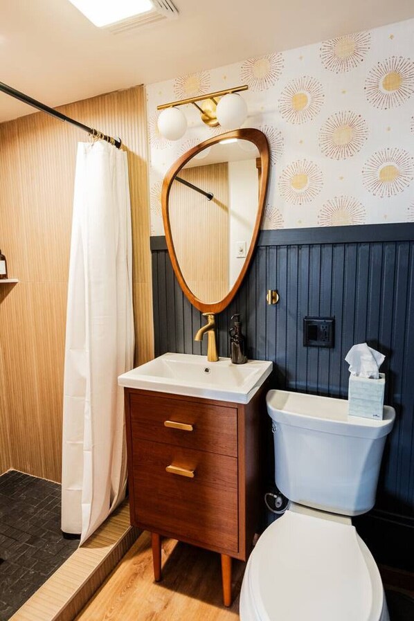 Un bagno con un mobile lavabo in legno, un lavandino bianco, un WC e una tenda per la doccia.