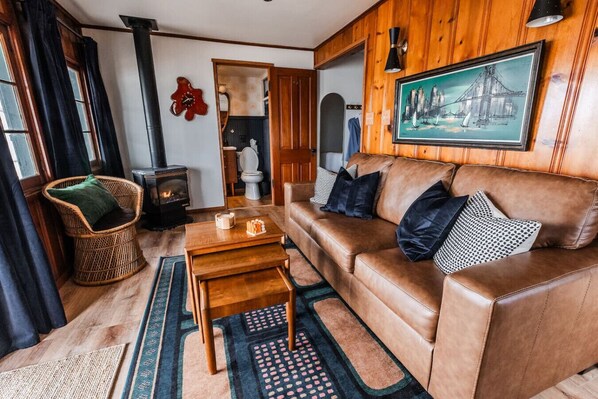 A cozy living room with a leather sofa, a wicker chair, a wooden coffee table, and a fireplace.