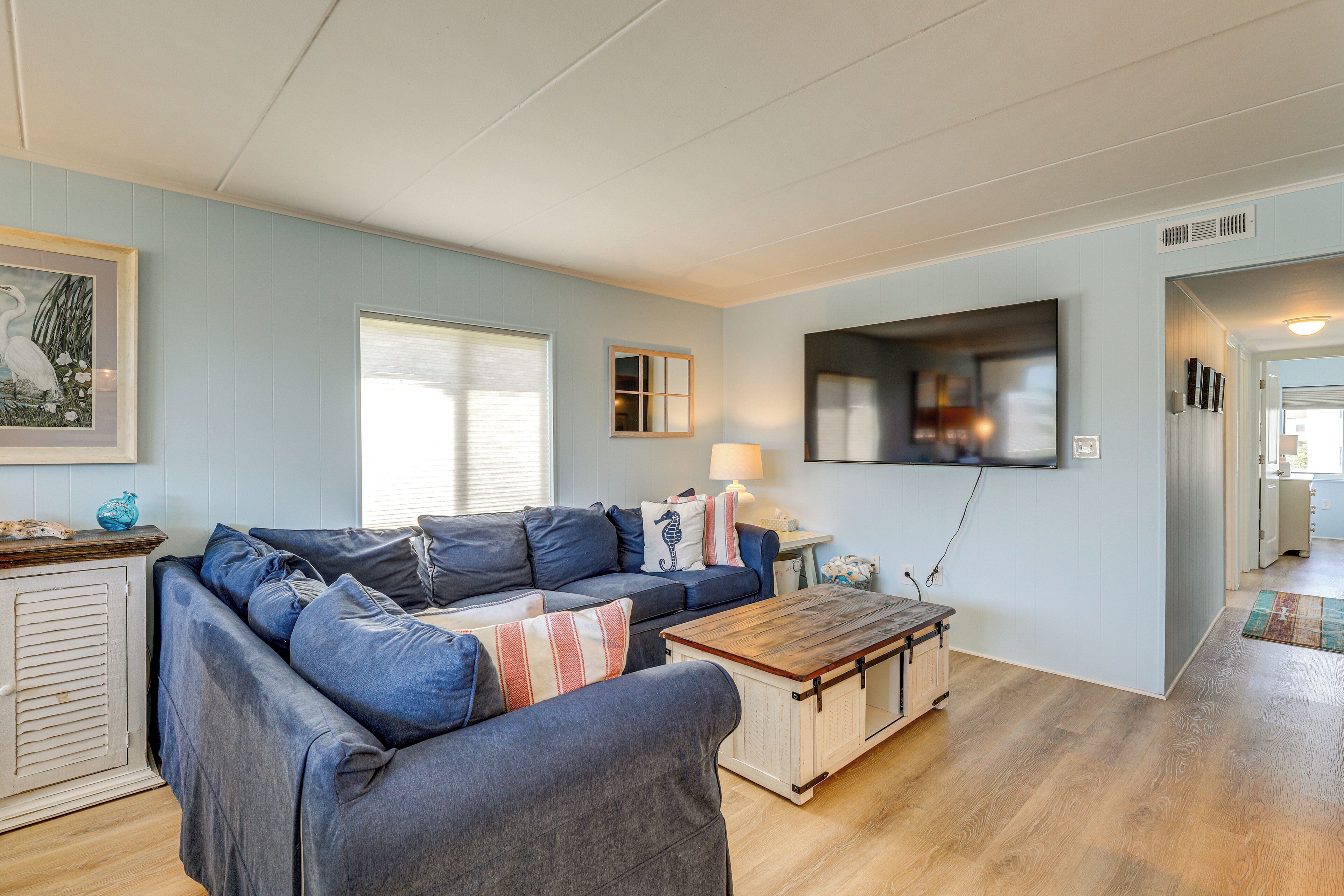 Un salon avec un canapé bleu, une table basse en bois et un téléviseur fixé au mur.