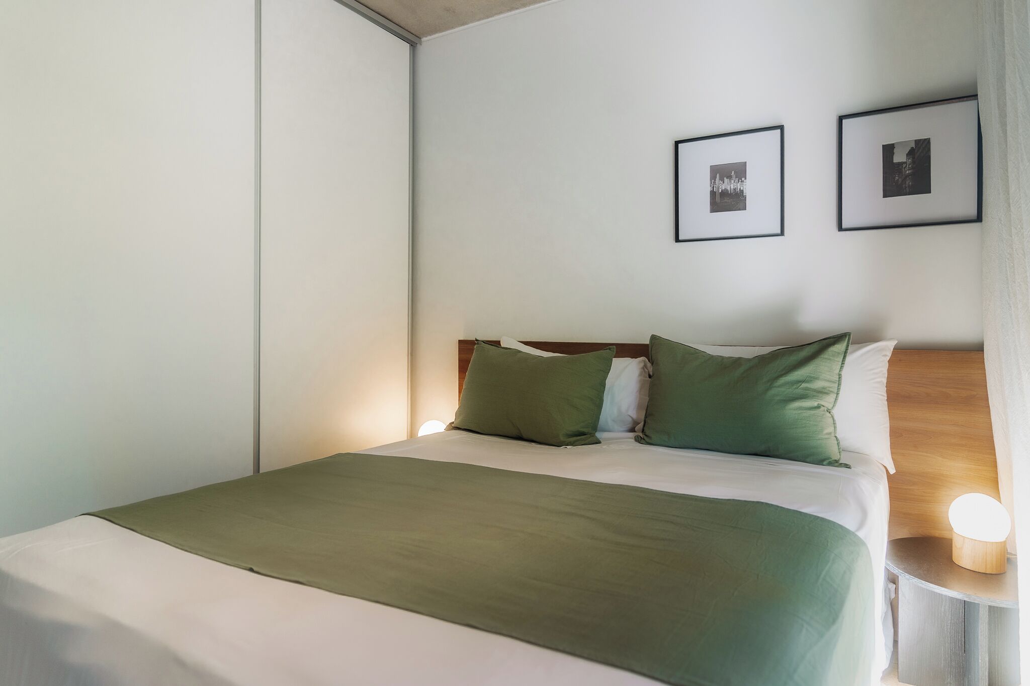 Ein ordentlich bezogenes Bett mit grüner Bettwäsche, einem hölzernen Kopfteil und zwei gerahmten Bildern an der Wand.