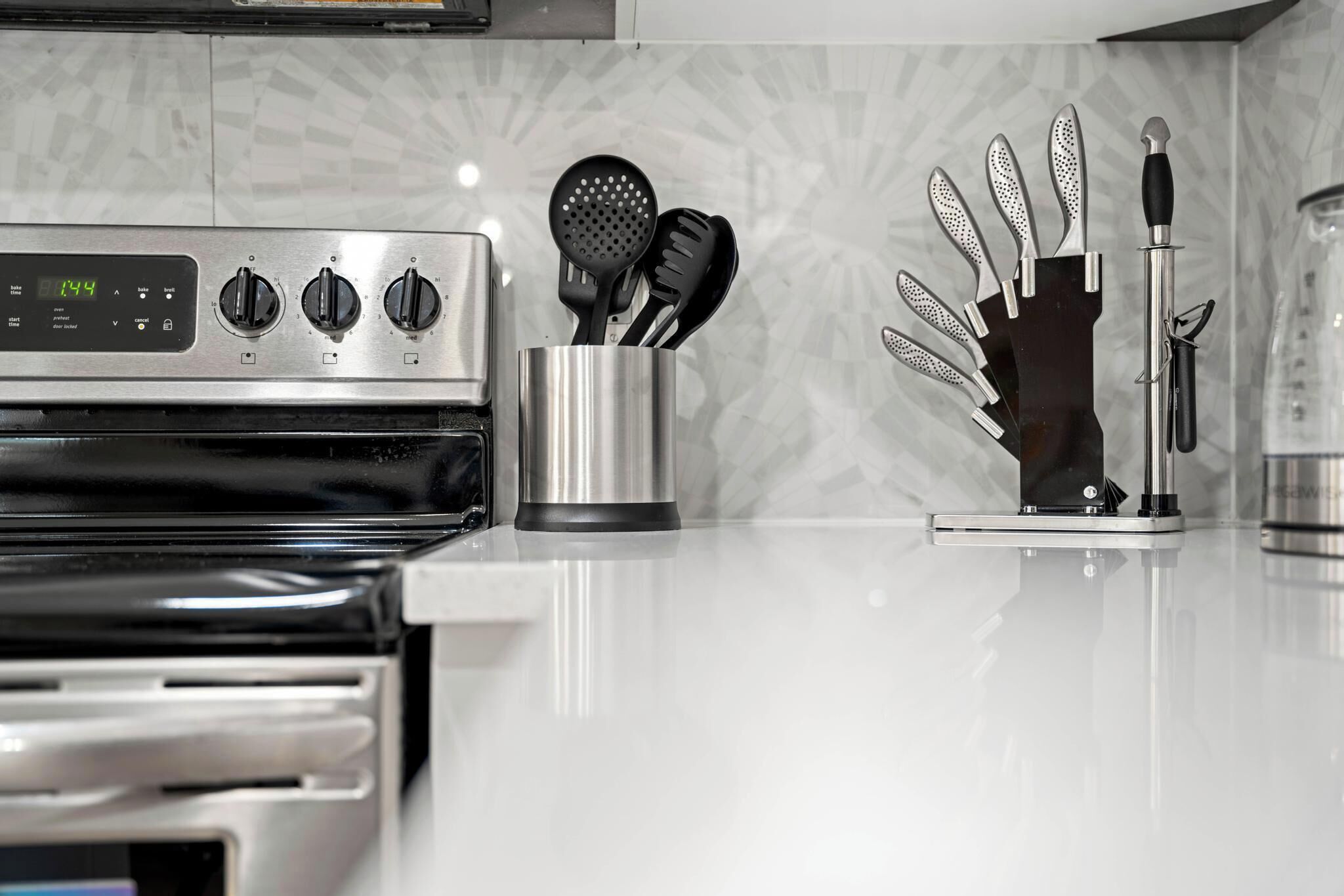 A kitchen with a stainless steel oven, a digital clock, and various utensils in holders.