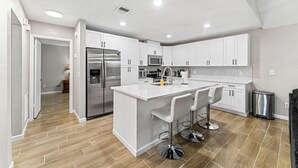 Una cocina moderna con armarios blancos, electrodomésticos de acero inoxidable y una isla central con taburetes de bar.