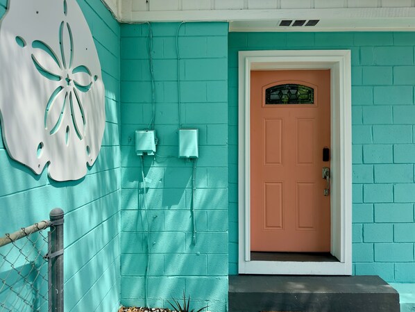 A teal house with a distinctive white door and a decorative wall piece.