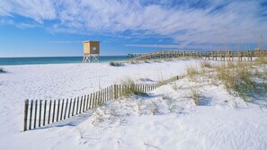 A sandy beach with a wooden lifeguard tower and a wooden pier extending into the water.