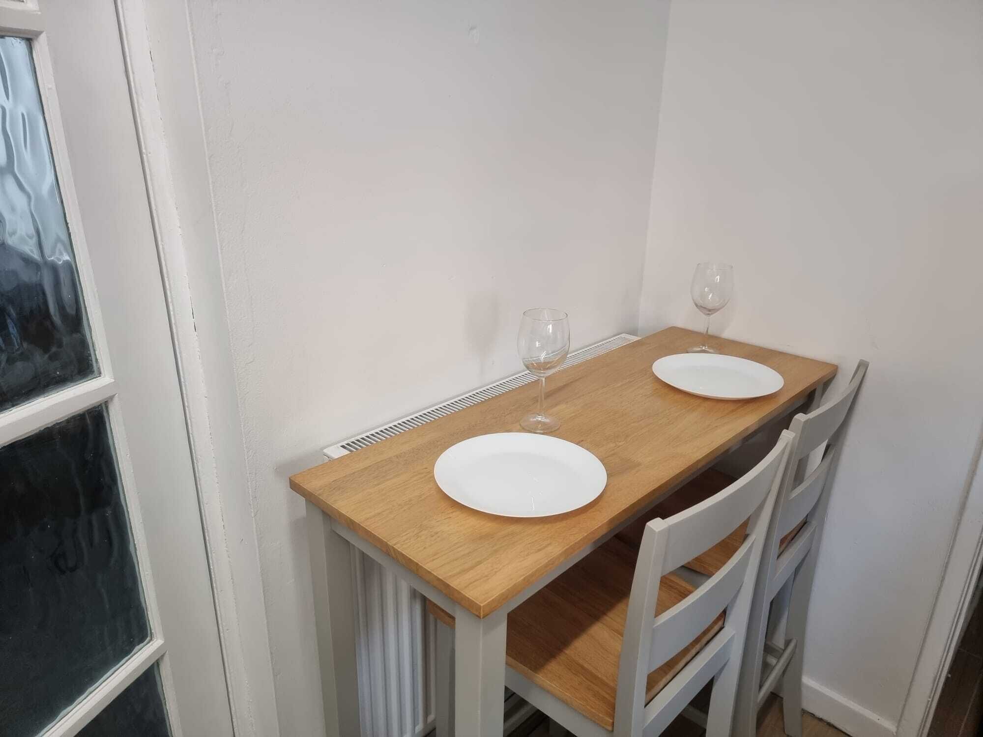 Een eettafel met twee witte borden en twee wijnglazen, omringd door witte stoelen.